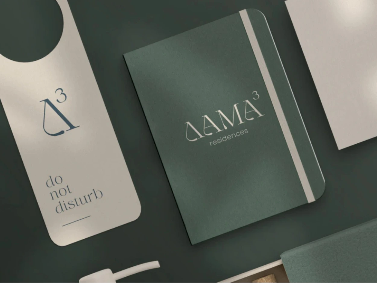 A do not disturb door hanger with the Δ³ mark next to a green notebook stamped ΔΑΜΑ³ residences